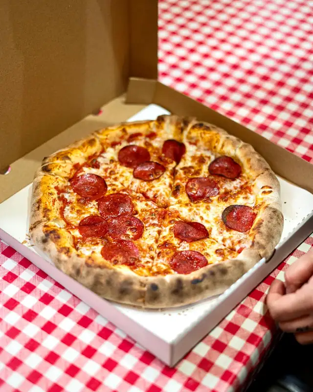 Pizza pepperoni w kartonie na czerwonym obrusie w kratkę